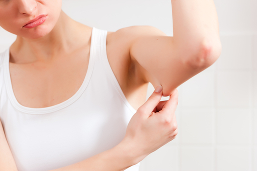 二の腕の脂肪をつまみ、悩んでいる女性の写真