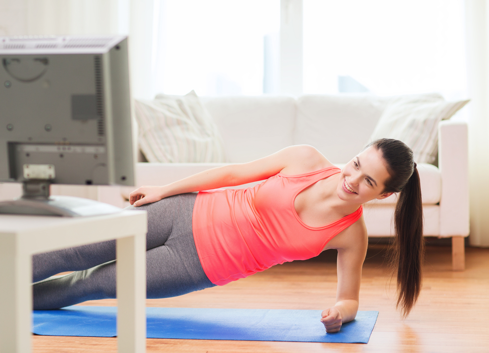 fitness, home and diet concept - smiling teenage girl doing side plank and watching tv at home
