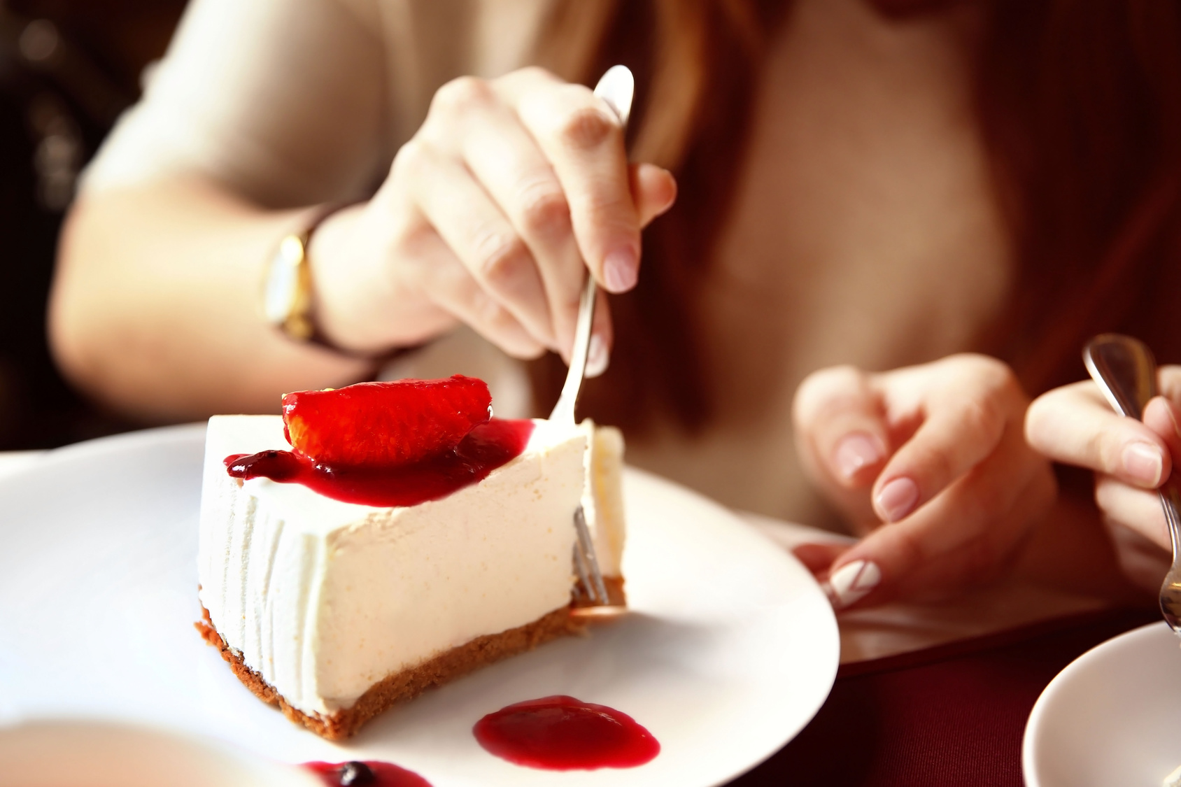 Woman eating tasty cheesecake on table in cafe or restaurant