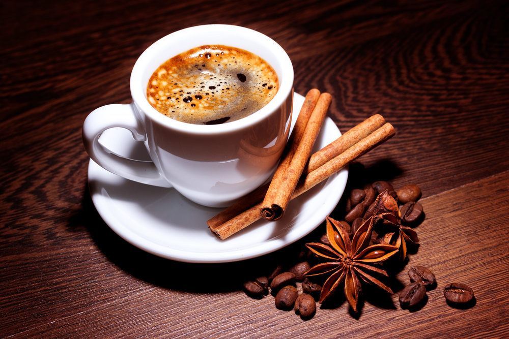 coffee in cup with milk, cinnamon and anise stars on wooden surface