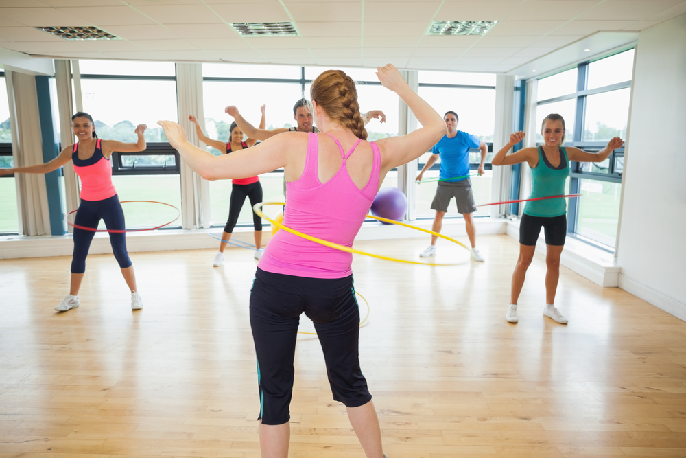 Fitness class and instructor swinging hula hoops at the waist in bright room